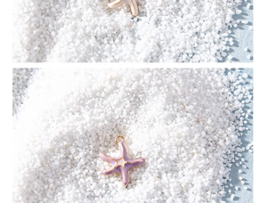 Macro view of purple starfish pendant with gold edges on white sand background