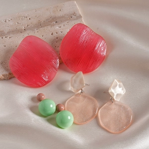 Detail of three pairs of textured resin earrings on beige silk and limestone base