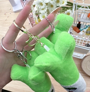 Close-up of a green plush spring onion keychain with gold metal buckle on wooden background