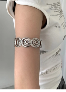 Macro detail of silver spiral upper arm cuff featuring a minimalist metallic swirl design