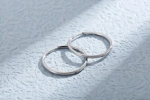 Macro shot of silver stainless steel hoop earrings with polished finish on blue textured background