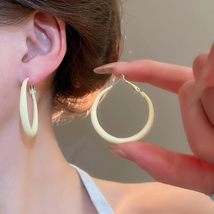 Close-up of cream-colored glossy hoop earrings worn by a model and held for detail