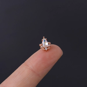 Macro detail of a rose gold cartilage stud with pear-shaped zircon on a fingertip