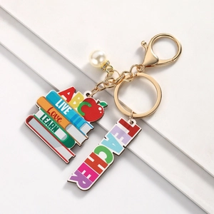 Close-up of a teacher-themed keychain with stacked books, pearl charm, and gold hardware