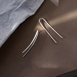 Elegant silver U-shaped minimalist drop earrings displayed on a brown leather surface