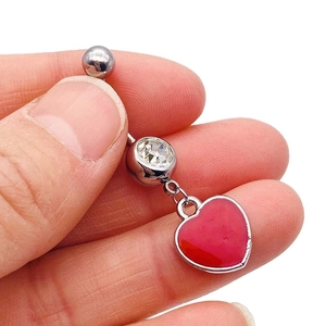 Silver stainless steel belly button ring with a red heart pendant held between fingers