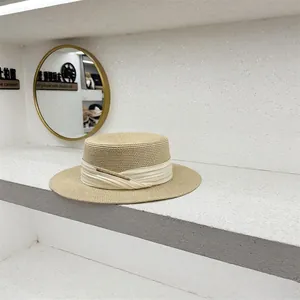 Detalle del sombrero de paja beige claro con cinta de raso blanco y hebilla dorada