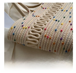 Detailed macro view of woven straw tote bag featuring colorful embroidery and wave rope trim