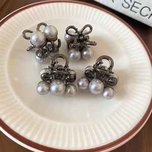Macro view of mini hair claw clips with bow details and pearls in a vintage ceramic tray