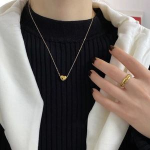 Parure collier cœur en or 18 carats et bague texturée portée par un mannequin élégant