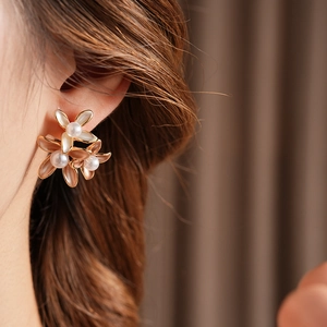 Detailed close-up of a gold flower earring with opal petals and a pearl center on a model