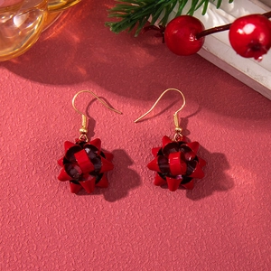 Detail shot of festive red bow earrings with gold hooks on a pine branch background