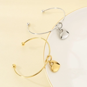 Detail view of gold and silver heart-shaped knot bangles on a textured warm background