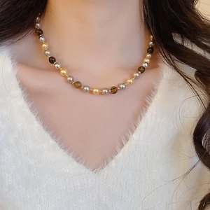 Gros plan du collier en perles d'oeil de tigre sur un mannequin en pull blanc à col en V