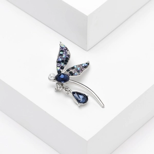 Detailed view of silver dragonfly brooch with blue crystals and a drop pendant