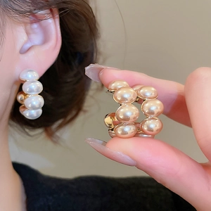 Detail of C-shaped gold-plated hoop earrings featuring elegant rows of white and champagne pearls