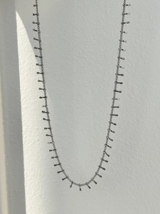 Detailed view of silver tone chain necklace with textured cylindrical charms and tassels
