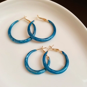 Nahaufnahme blauer Creolen aus Marmorharz mit goldenen Metalldetails auf Keramikschale