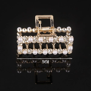 Detail showing a 5cm golden geometric hair claw with pearls and rhinestones on black
