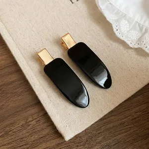 Elegant pair of black and gold teardrop hair clips on a textured fabric and wood surface