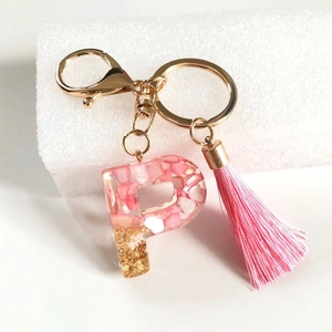 Detailed close-up of pink resin letter P keychain with gold foil and tassel accent