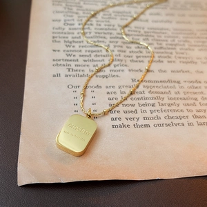 Macro detail of golden square pendant engraved with CHARM on a vintage paper backdrop