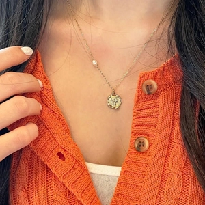 Detail of a gold coin pendant necklace with a white pearl on an orange knit sweater