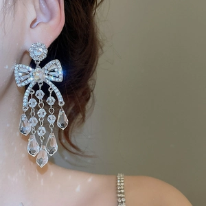 Close-up of dangling bow tassel earrings with sparkling crystals on a female model
