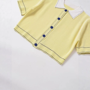 Pale yellow polo knit cardigan with white collar and dark blue buttons on white background