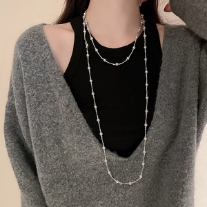 Détail d'un long collier à billes argentées superposé sur un gilet en maille grise