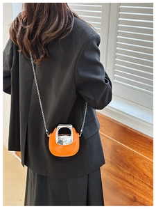 Detail of a mini orange crossbody bag with a distinctive silver D-shaped metal handle