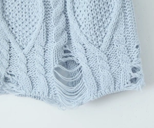 Close-up of light blue knit sweater showing cable knit pattern and distressed hole details