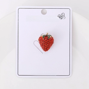 Detail showing a strawberry brooch with red crystals and green leaves on a jewelry card