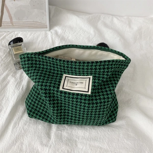 Detail of green houndstooth makeup bag featuring a top zipper and woven fabric label