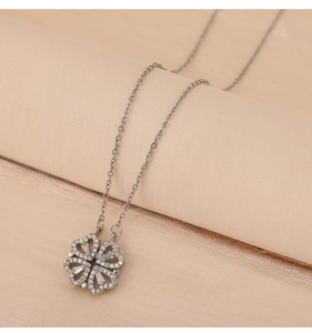 Detail of silver clover necklace with zircon inlay on a beige silk scroll surface