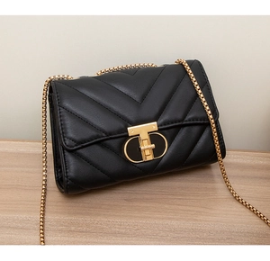 Detail of black quilted leather shoulder bag with gold chain and metal lock on wooden table
