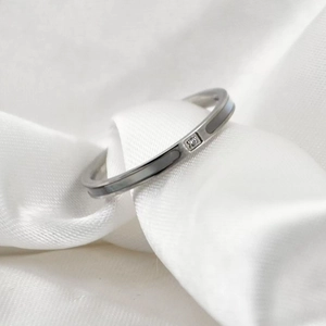 Macro shot of minimalist silver titanium steel ring with dark inlay and zircon on white silk