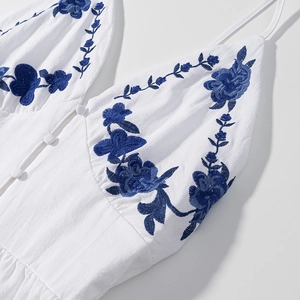 Close-up of blue flower embroidery and cloth buttons on white cotton linen dress