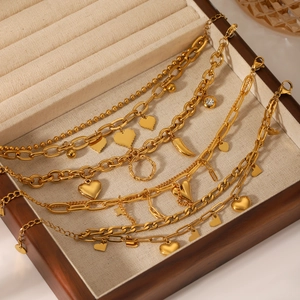 Detail of gold chain bracelets with heart and star charms on beige velvet jewelry box