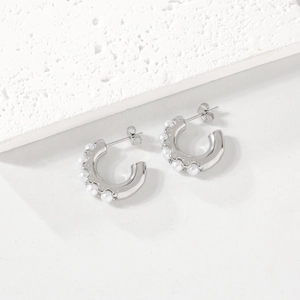 Silver C-shaped stainless steel earrings with white pearls on a textured stone background