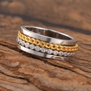 Macro shot of silver spinner ring with gold rope pattern and zircon inlay on rustic wood