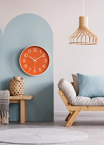 Modern orange wall clock with white digits displayed on a blue minimalist interior wall