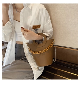 Close-up of brown bucket bag with resin chain detail and round handle on model