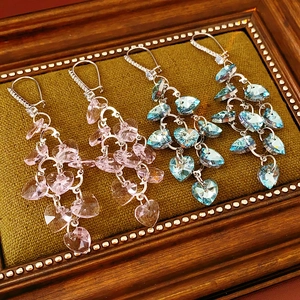Detailed macro view of pink and blue crystal heart tassel earrings on green fabric
