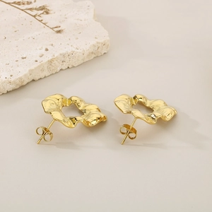 Macro view of golden irregular wavy stud earrings on white textured stone background