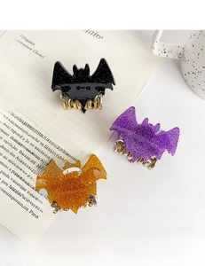 Close-up of three glittery Halloween bat hair claws in black, purple, and orange on a book