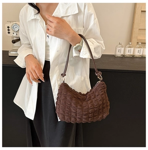 Detail of dark brown bubble textured fabric and slim shoulder strap on an underarm bag