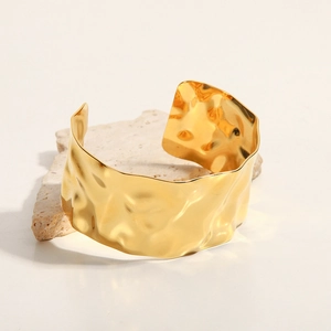 Detailed close-up of a wide hammered 18K gold-plated cuff on a textured stone