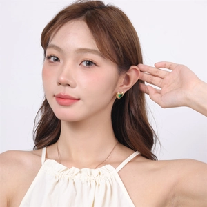 Detail shot of heart-shaped green crystal earrings and gold necklace on model
