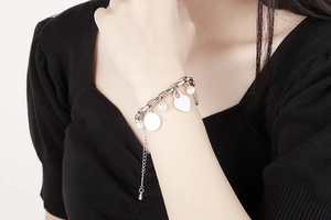 Bracelet chaîne argenté avec pendentifs cœur, rond et perles sur un poignet féminin